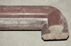 Close-up of a brown wooden banister handrail showing a rounded corner joint and worn surface details.