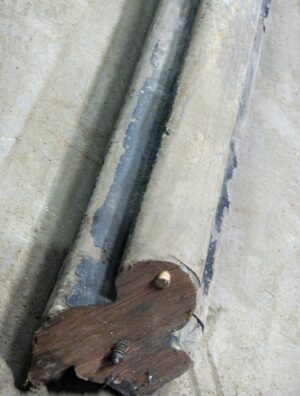 Close-up of a reclaimed wooden banister with a wide base and thin handrail, shown at an angle with visible wear and a black-painted section.