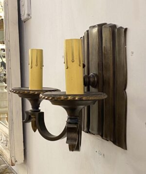 Traditional bronze two-arm wall sconce with candle-style bulb sleeves and an antique bronze finish, shown in a close-up view of one side of the fixture.