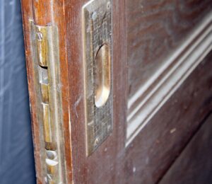 Close-up of a pocket door edge showing the brass latch hardware and the glass insert frame on a dark wood-toned door.