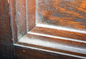 Close-up of a dark wood tone pocket door corner with paneled sections and worn grain details, showing the raised frame and edge joinery.