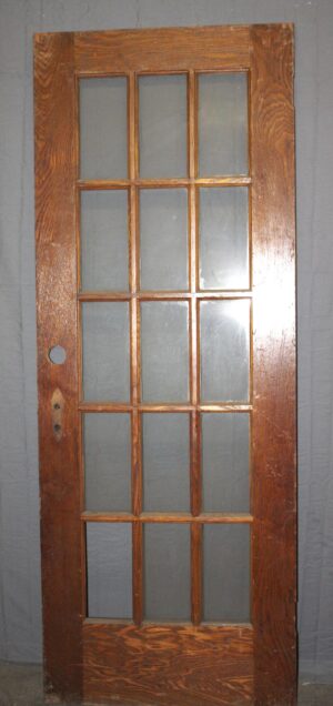 Antique 15-lite oak French door shown upright, with fifteen glass panes and one missing pane visible near the lower left side.