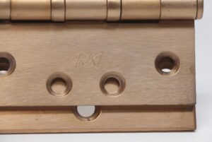 Close-up of a vintage McKinney 4 x 4 bent door hinge in antique brass finish, showing the five knuckles, mounting holes, and worn surface wear.