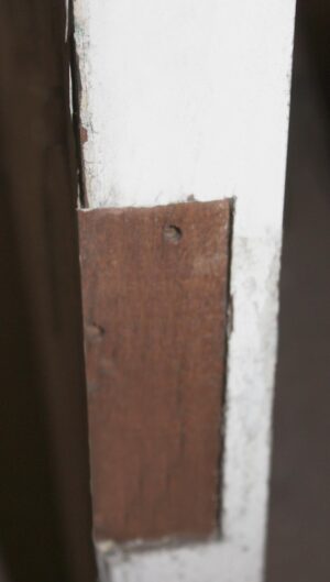 Close-up of a white wood passage door showing a weathered rectangular hardware patch with a screw hole.
