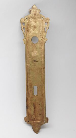 French-style bronze door back plate with a central keyhole cutout and decorative top and bottom ends, shown in full length with visible surface wear from prior use.
