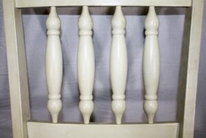 Close-up of a white wood chair frame with turned back spindles and a missing seat.