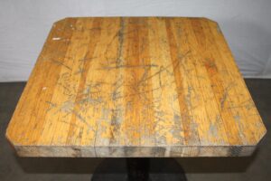 Close-up of a butcher block table top with visible scuffs and wear, shown from above.