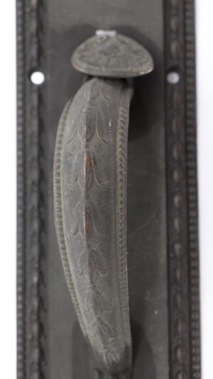 Close-up of an antique bronze entry door pull with leafy handle detail and a thumb latch and lock insert visible.