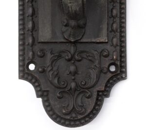 Close-up of an antique bronze neoclassical door pull with a leafy scroll design, showing the lower section with two mounting holes and the decorative thumb latch area.