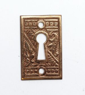 Ornate brass keyhole cover plate with an Aesthetic pattern and one large keyhole opening, shown front on.
