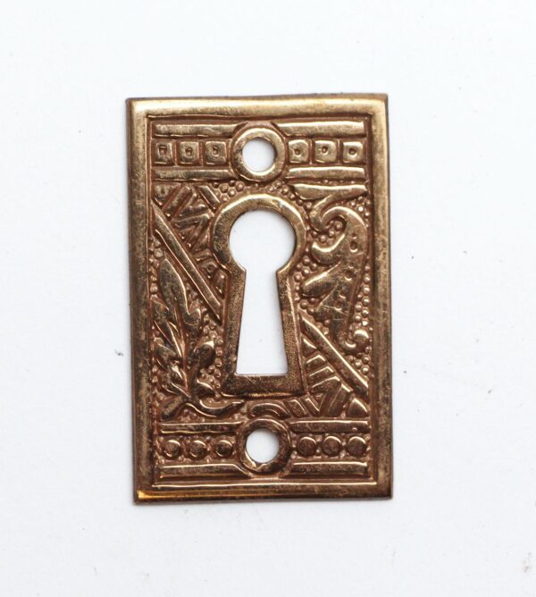 Ornate brass keyhole cover plate with an Aesthetic pattern and one large keyhole opening, shown front on.