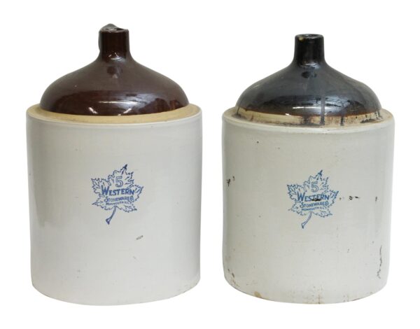 Pair of ceramic stoneware jars with white bodies, one with a brown top and one with a black top, both stamped with a blue Western Stoneware Co. mark.
