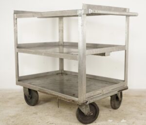 Three-tier stainless steel service cart with handle and four casters, shown in a three-quarter view with visible scratches, dents, and worn edges.