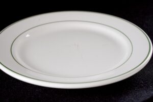 White round dinner plate with green trim, shown from above with light surface wear.