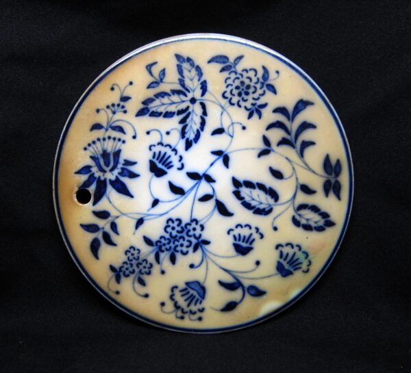 Round ceramic trivet with a blue floral pattern and a small hanging hole near the edge.