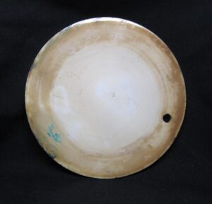Round ceramic trivet with a small hanging hole near the edge, shown in blue and white with visible wear.