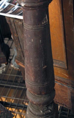 Close-up of a traditional wooden staircase newel post with a dark wood tone and carved bulls eye detail.