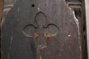 Close-up of an antique oak staircase newel post showing a carved Gothic cross design.