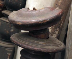 Close-up of a traditional wooden newel post with a removable top piece, shown in a dark wood tone and worn, restorable condition.