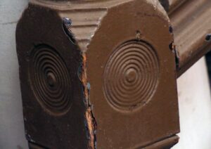 Close-up of a carved wooden staircase newel post with bulls eye circular details and visible wear on the edges.