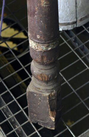 Close-up of a brown wooden staircase newel post with a carved ball detail and visible wear on the lower section.