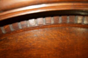Close-up of an arched door pediment with dentil molding in a dark wood tone.