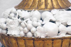 Close-up of a vintage table lamp showing the gilt base and white ceramic fruit decoration.