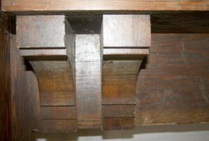 Close-up of an oversized mantel showing a carved wood bracket with a dark wood tone and visible patina.