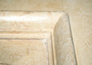 Close-up of a mirrored wood closet door showing the corner of one panel and frame with a tan and white painted surface.