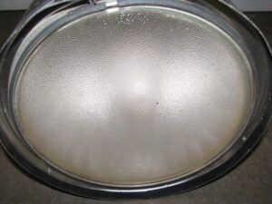 Close-up of a round industrial light with a pebbled Fresnel lens and black steel rim.