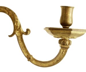 Close-up of an antique brass wall sconce with a curved arm, candle cup, and decorative mount.