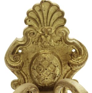 Close-up of an antique French brass wall sconce backplate with ornate scroll and shell detailing and two mounting holes.