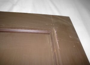 Close-up of a brown wood passage door showing the upper corner and trim of one of its two panels.