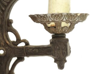 Close-up of an ornate Victorian wall sconce with one candle-style holder, showing the cast metal arm and decorative backplate in black finish.