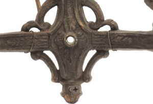 Close-up of an ornate Victorian wall sconce in black metal, showing the central decorative mount and one screw hole.