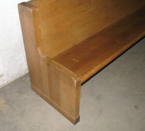 Close-up of a solid oak bench end and seat with a curved side panel and visible surface wear.