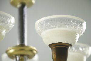 Close-up of a Victorian five-arm chandelier with clear and frosted slip shades and a mixed nickel and antique brass finish.