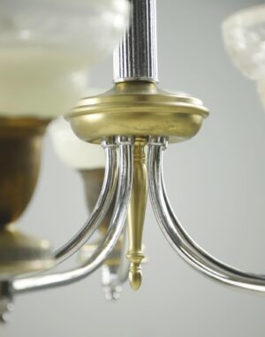 Close-up of a chandelier arm with nickel and antique brass finish, showing the central canopy and curved arms.