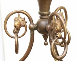 Close-up of a brass pendant ceiling lantern with griffin head details and circular loops, showing the central fitting and part of the suspended frame.