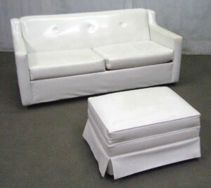 White mid-century two-seat sofa with matching ottoman in a simple upholstered design.