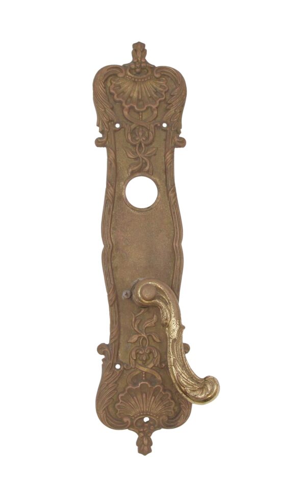 Art Nouveau brass door lever set with an elongated back plate, scalloped and vine detailing, and a serpentine lever handle.
