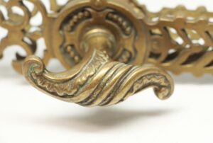 Close-up of a bronze door handle with a serpentine lever and ornate cutout back plate, showing the decorative curved grip and worn antique gilt finish.