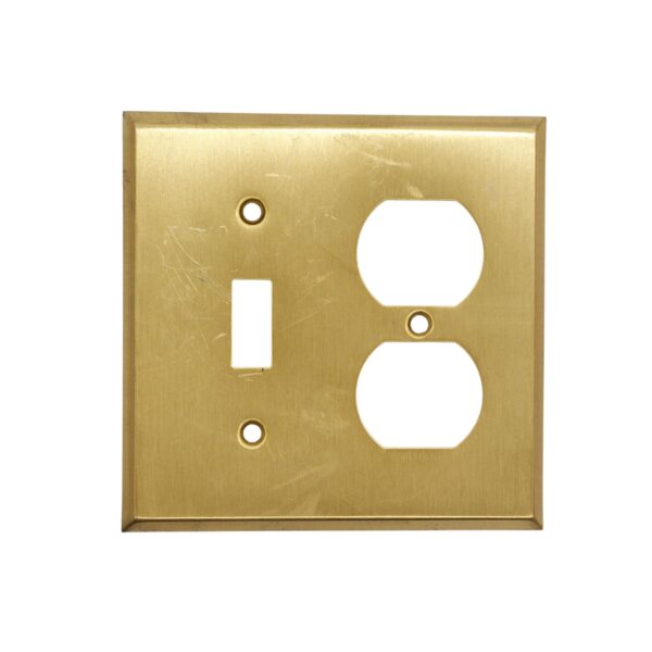 Brushed brass wall plate cover with one toggle switch opening, one duplex outlet opening, and two screw holes, shown with surface wear from prior use.