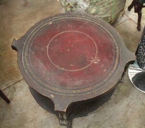 Round wooden side table with a worn leather-inlaid top and visible edge chipping.