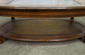 Oval oak coffee table with a cutout glass center and a cane-pattern lower shelf, shown from a low angle.