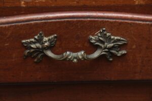 Close-up of a wooden drawer front on a side table with an ornate metal handle in a dark wood tone.