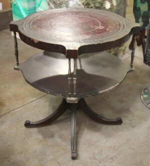 Antique round wooden side table with a leather-inlaid top and visible edge chipping, shown with a lower shelf and curved legs.