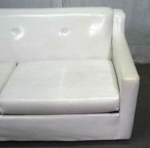 White mid century vinyl sofa shown in close-up, with a tufted backrest and right armrest visible.