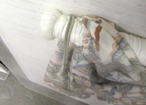 Preserved Japanese obi garment with patterned fabric secured in an acrylic box frame, shown in close-up with the mounting hardware visible on the back.