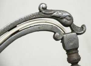 Close-up of an antique floor lamp top with a horse motif and curved metal arm, showing the upper section and connector detail.
